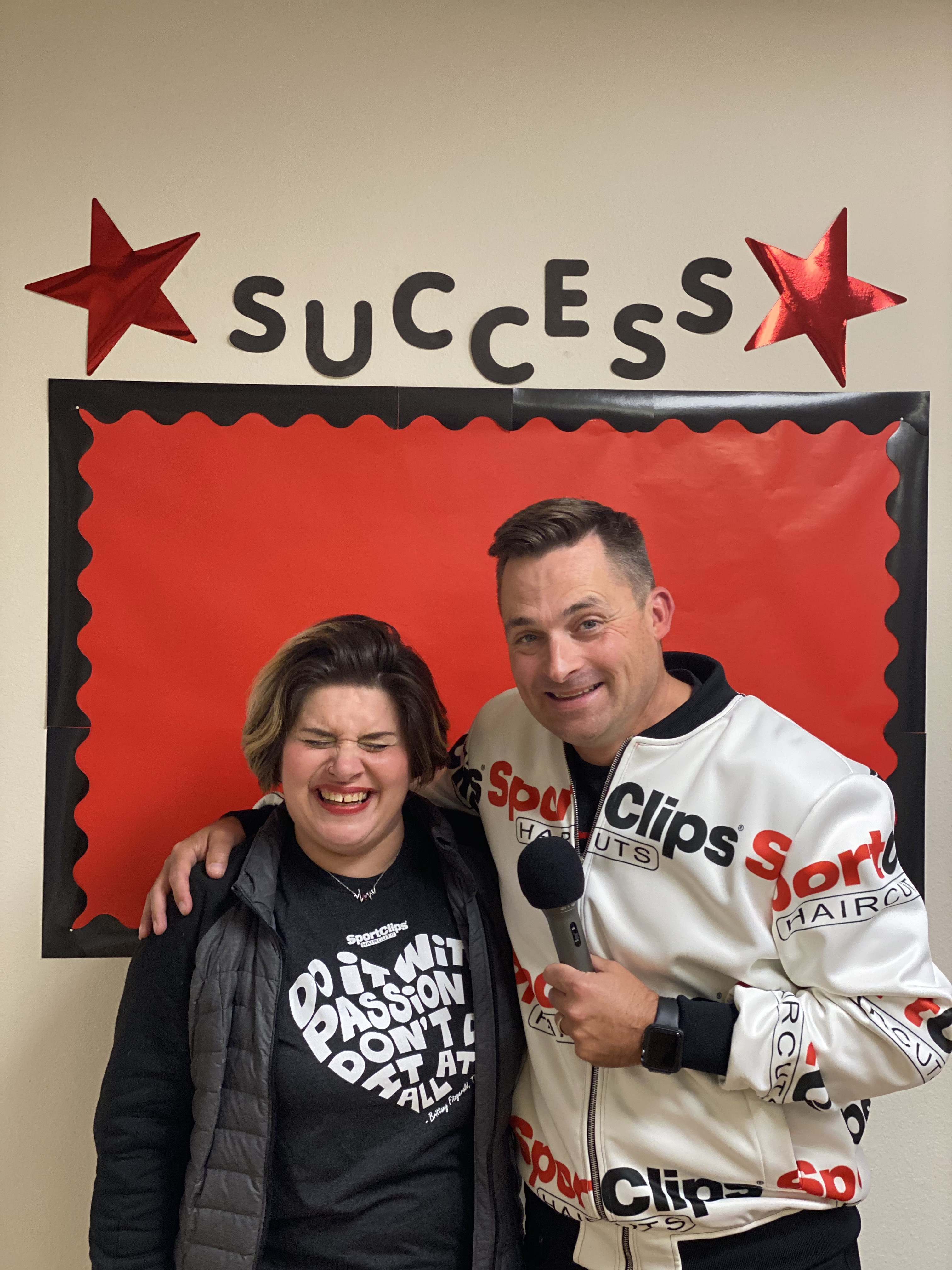 Chad Jordan in a Sport Clips Jacket and Veronica Jordan holding a microphone laughing